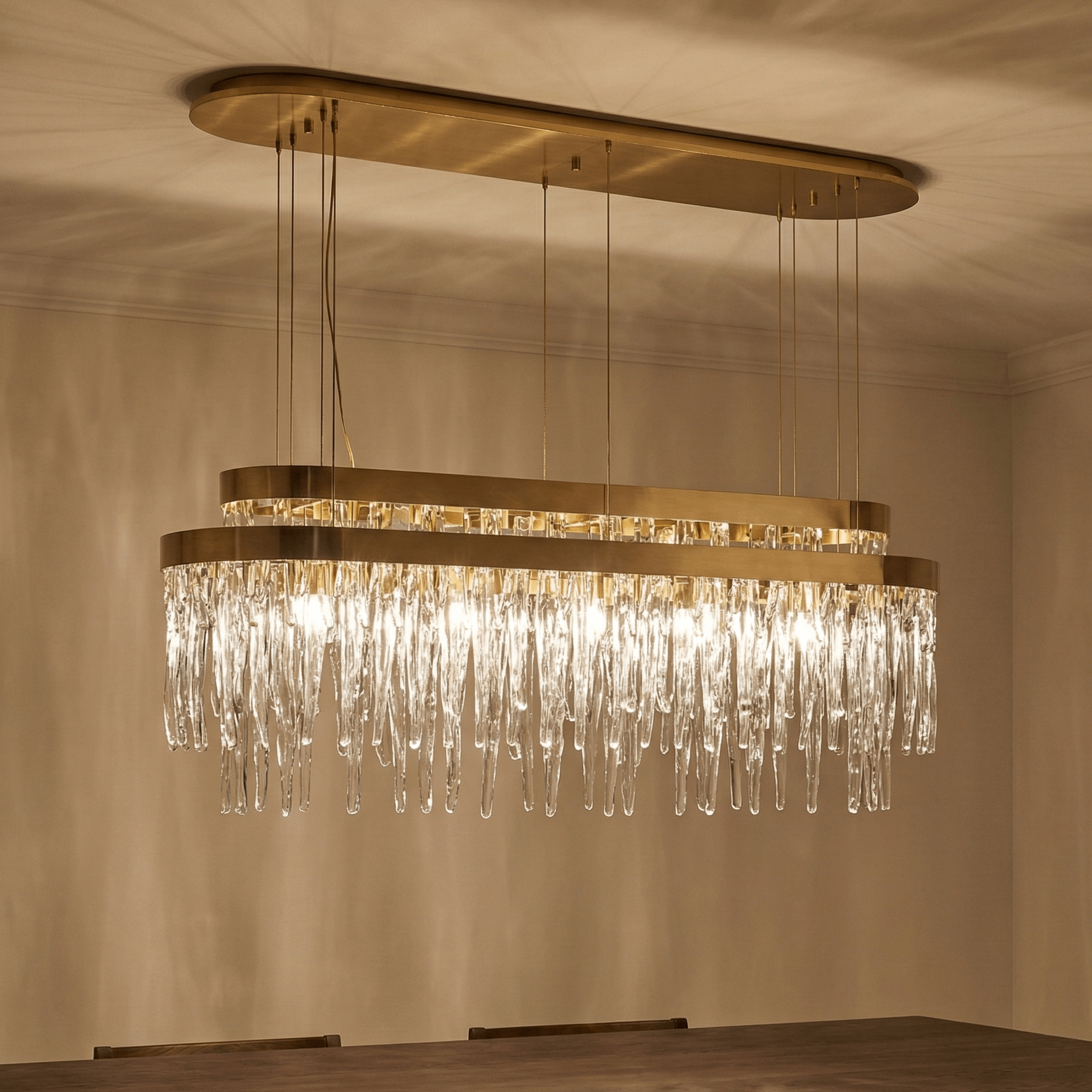 Luxury rectangular crystal chandelier with brass finish illuminating a modern dining room, suspended above a solid wood dining table with warm ambient lighting and elegant shadows.