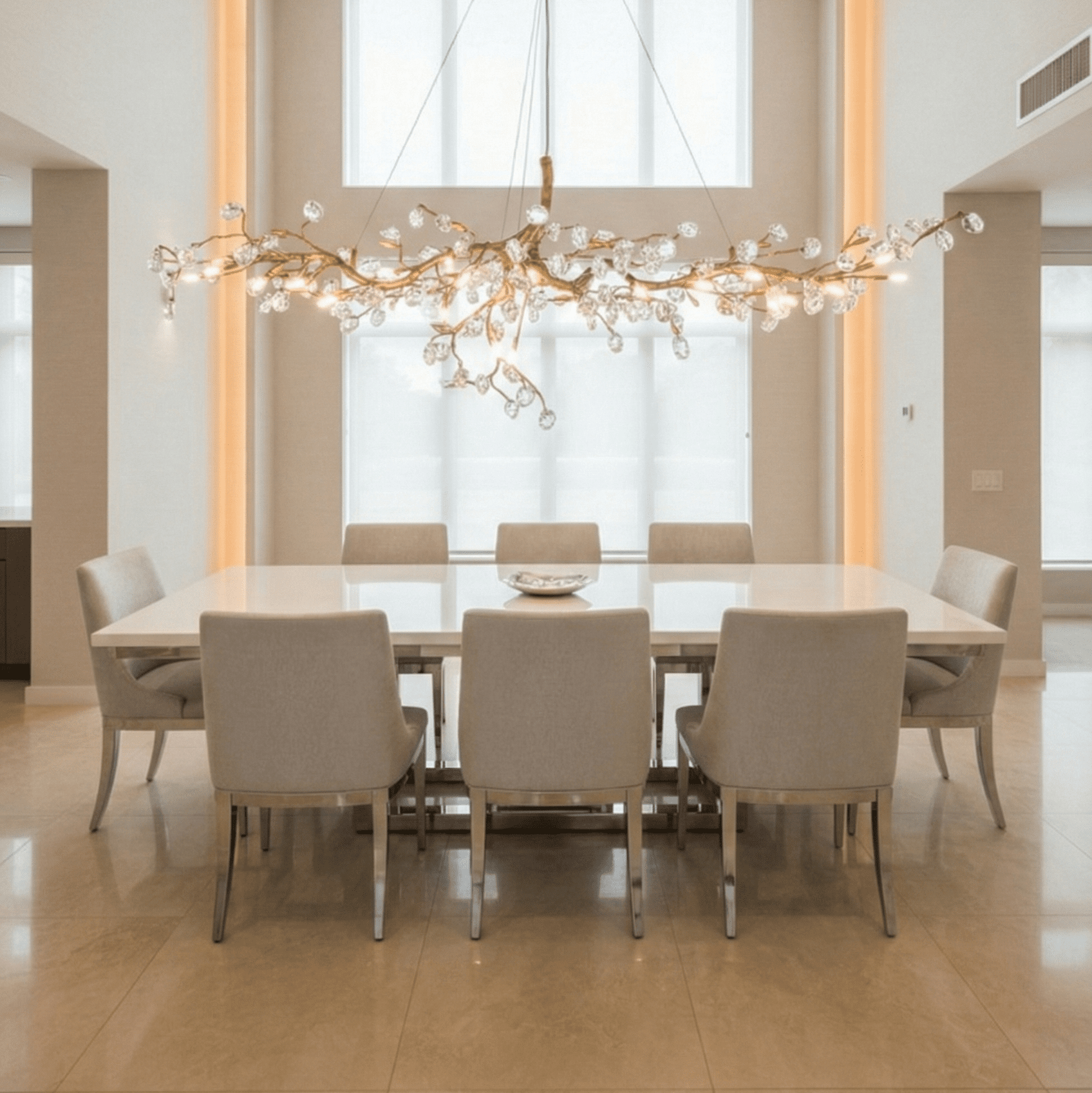 Luxury modern branch chandelier in gold finish with crystal glass details, installed above a contemporary dining table in an elegant minimalist dining room