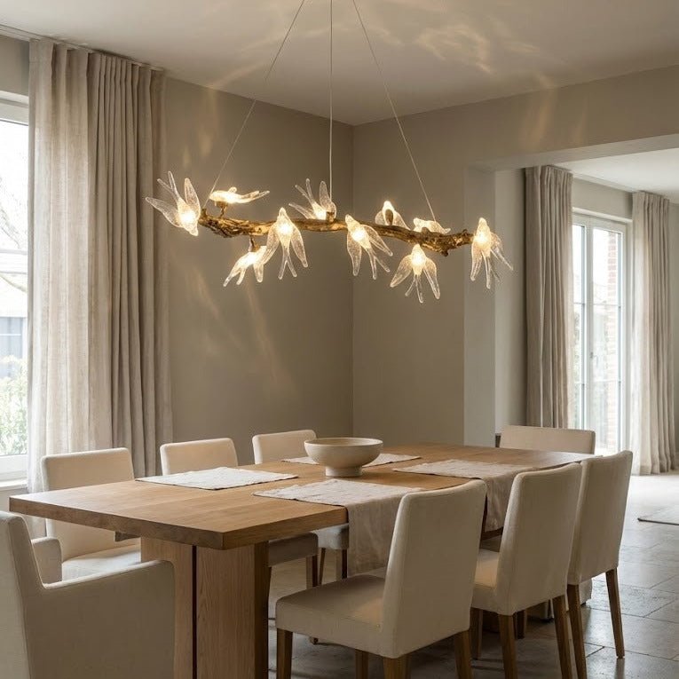 Antique brass glass bird chandelier suspended above a modern dining table, featuring hand-cast branch-style frame and illuminated crystal bird details in a luxury dining room interior