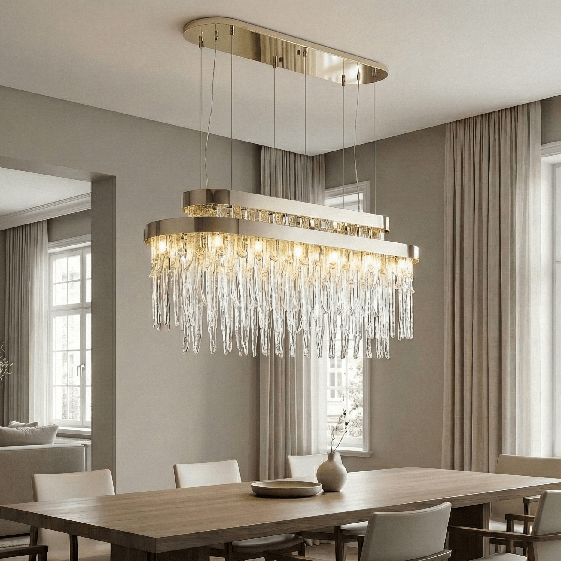 Modern polished nickel rectangular crystal chandelier centered above a large dining table in a bright contemporary dining room with soft natural light and neutral decor.